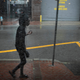A woman wearing a black rain jacket walks down a street in front of a sign during heavy rains.